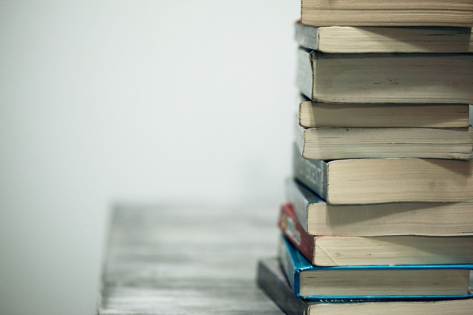 A stack of well-read paperback books on a wooden table