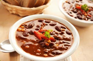 A white bowl of chili with beans, topped with red chili peppers and a sprig of parsley