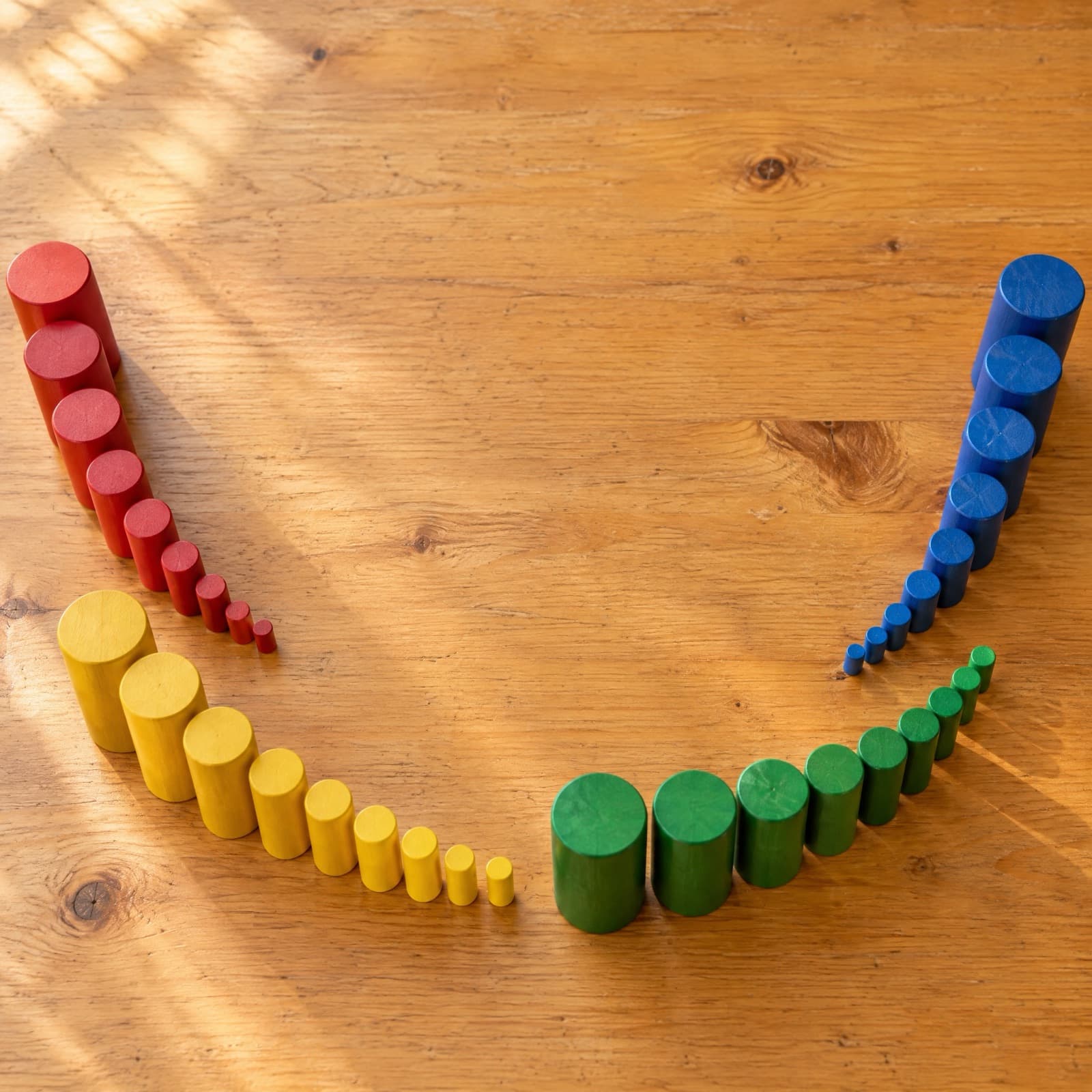 Montessori knobless cylinders in red, yellow, green and blue, arranged from largest to smallest on a wooden floor